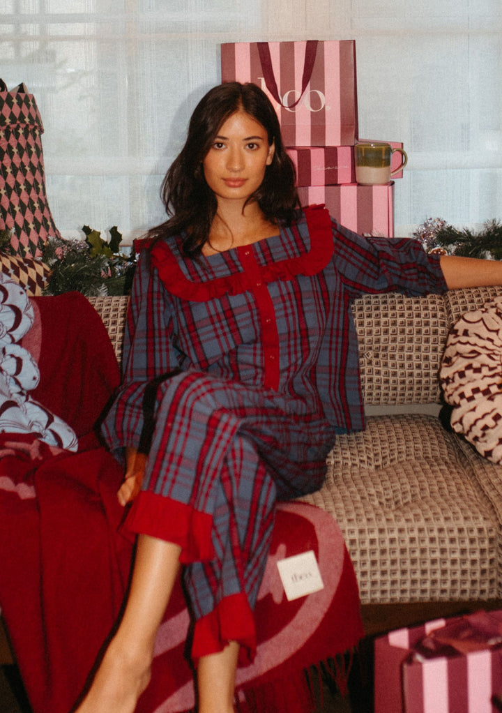 Woman relaxing indoors wearing TBCo Cotton Pyjamas in Navy Tartan with ruffle collar and cropped trousers