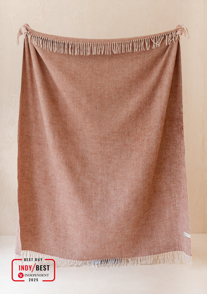 TBCo Recycled Wool Blanket in Rust Waffle with fringed edges, displayed hanging against a cream wall showing textured weave pattern