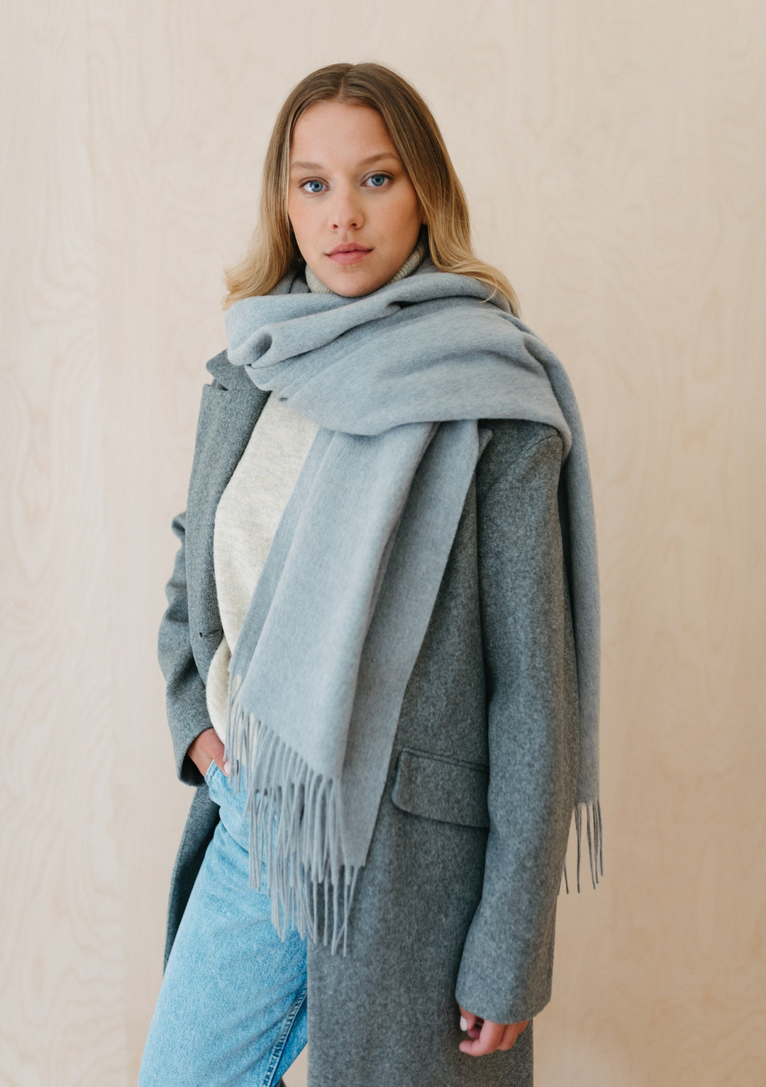 Luxuriously soft TBCo Lambswool Oversized Scarf in Light Grey Melange draped stylishly over a grey winter coat, showcasing fringed detail