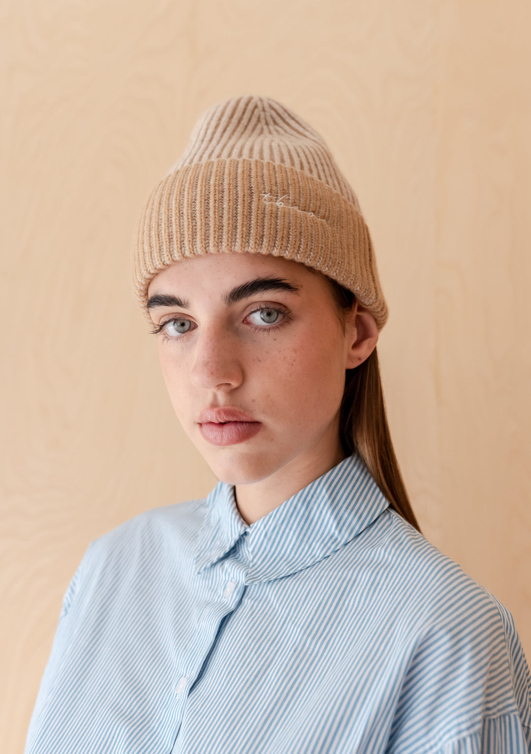 Woman wearing TBCo Cashmere & Merino Beanie in Oatmeal Two-Tone with embroidered logo and blue striped shirt