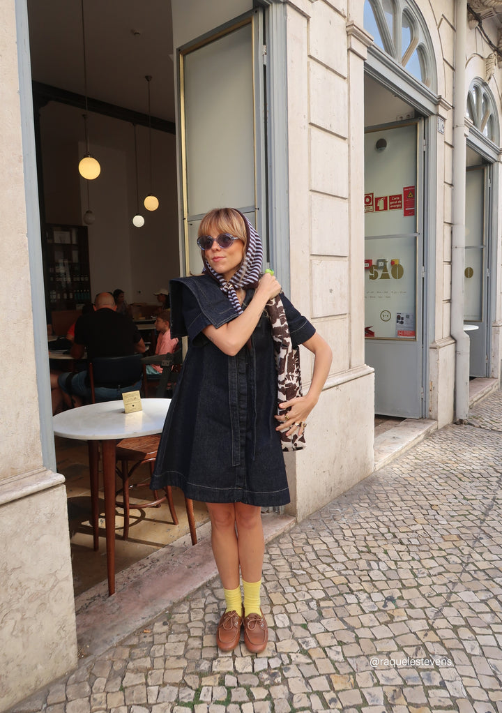 Woman wearing a TBCo Merino Wool Triangle Scarf in Blue & Brown Stripe styled with sunglasses and a black dress outside a café