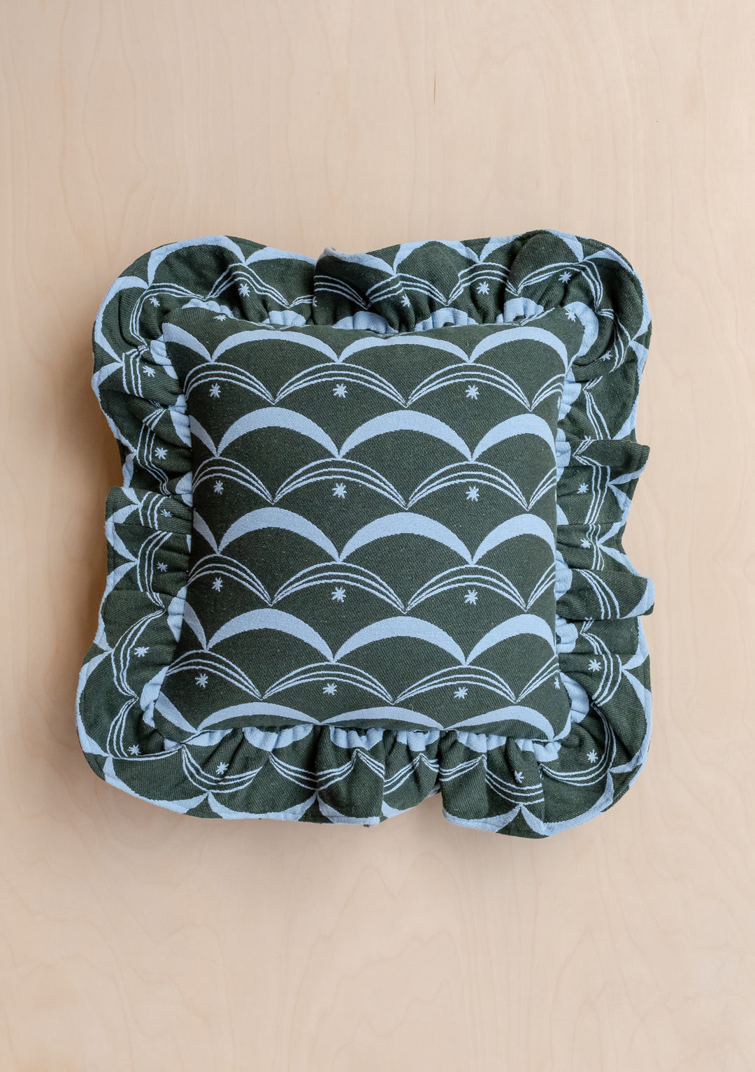 TBCo Cotton Cushion Cover in Green Circus featuring a dark green fabric with pale-blue scallop pattern, star motifs, and a ruffled edge, resting on a light wood surface.