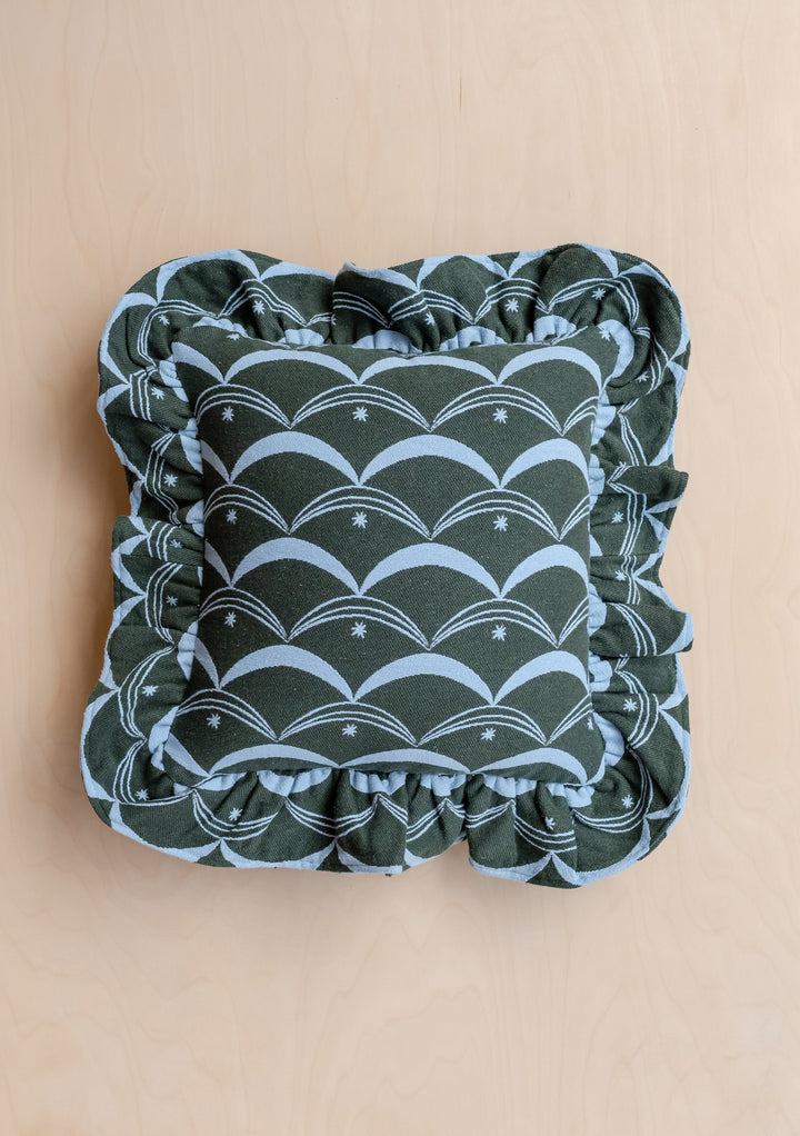 TBCo Cotton Cushion Cover in Green Circus featuring a dark green fabric with pale-blue scallop pattern, star motifs, and a ruffled edge, resting on a light wood surface.