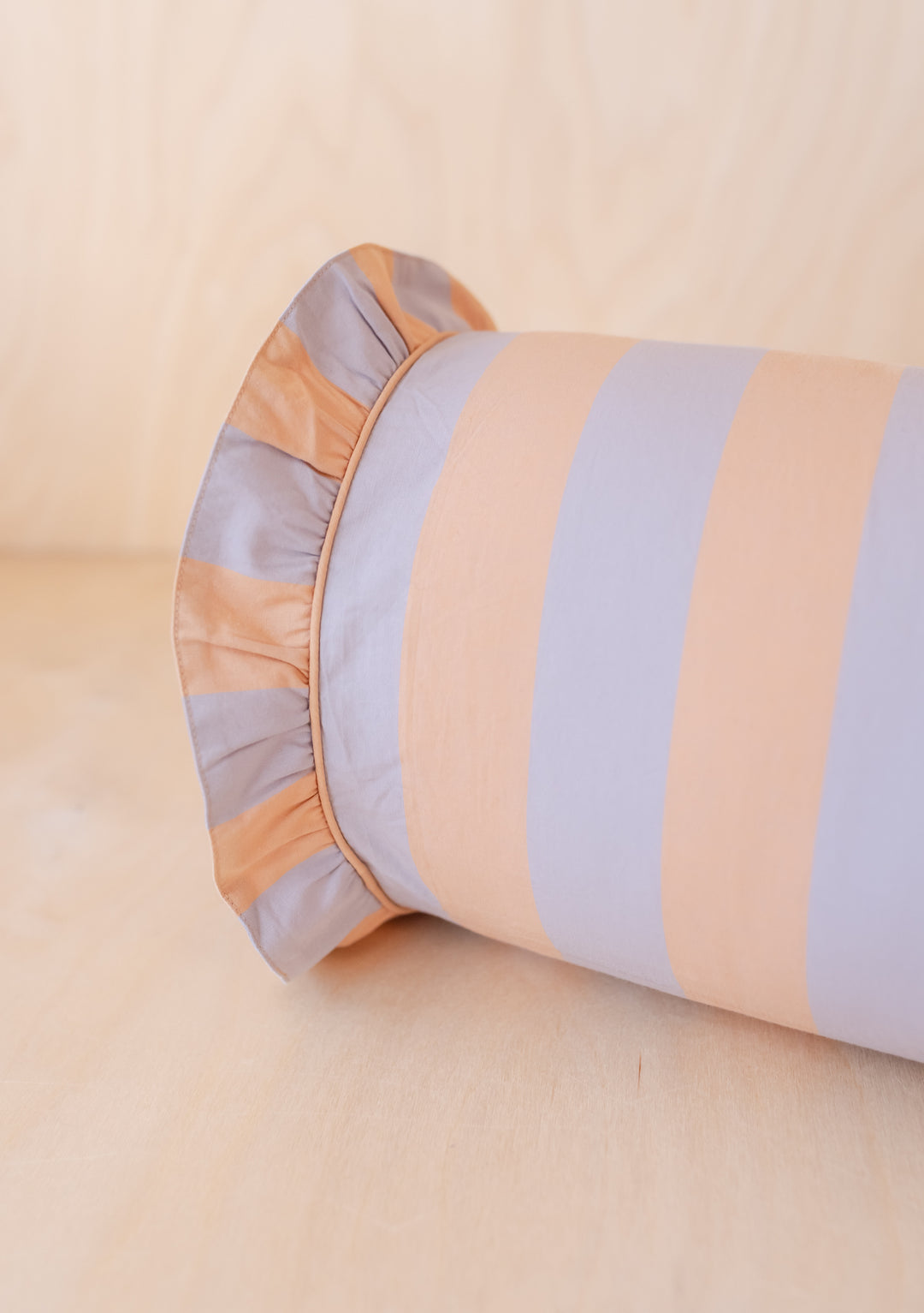 TBCo Cotton Bolster Cushion Cover featuring orange and lilac stripes with ruffle trim, photographed on wooden surface
