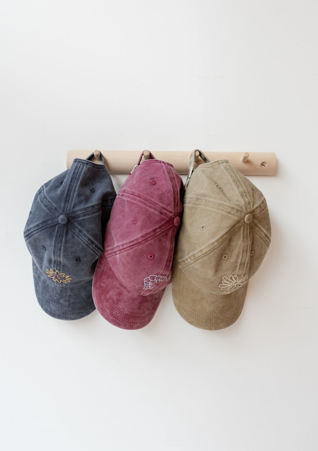 TBCo Recycled Cotton Cap in Sun displayed with other caps, showing embroidered floral detail on adjustable cotton headwear
