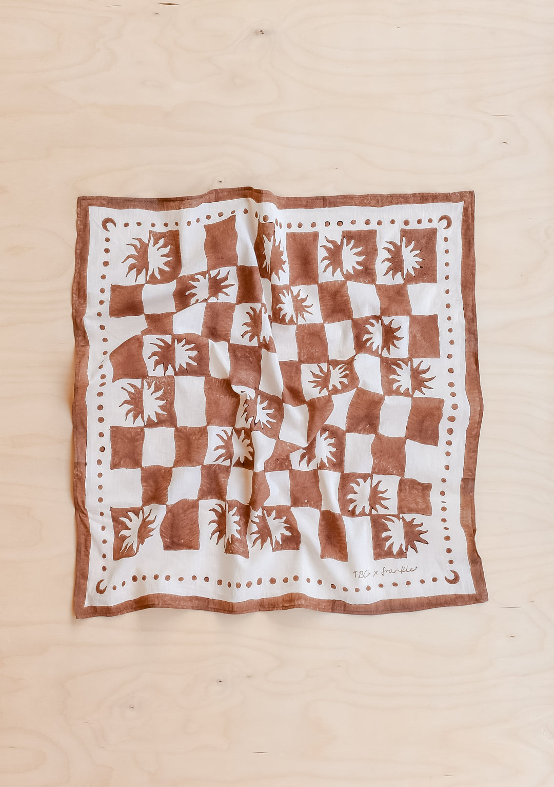 The Artist Series TBCo x Frankie Penwill Cotton Scarf features a checkerboard of sunburst motifs and a dotted border on a square fabric.