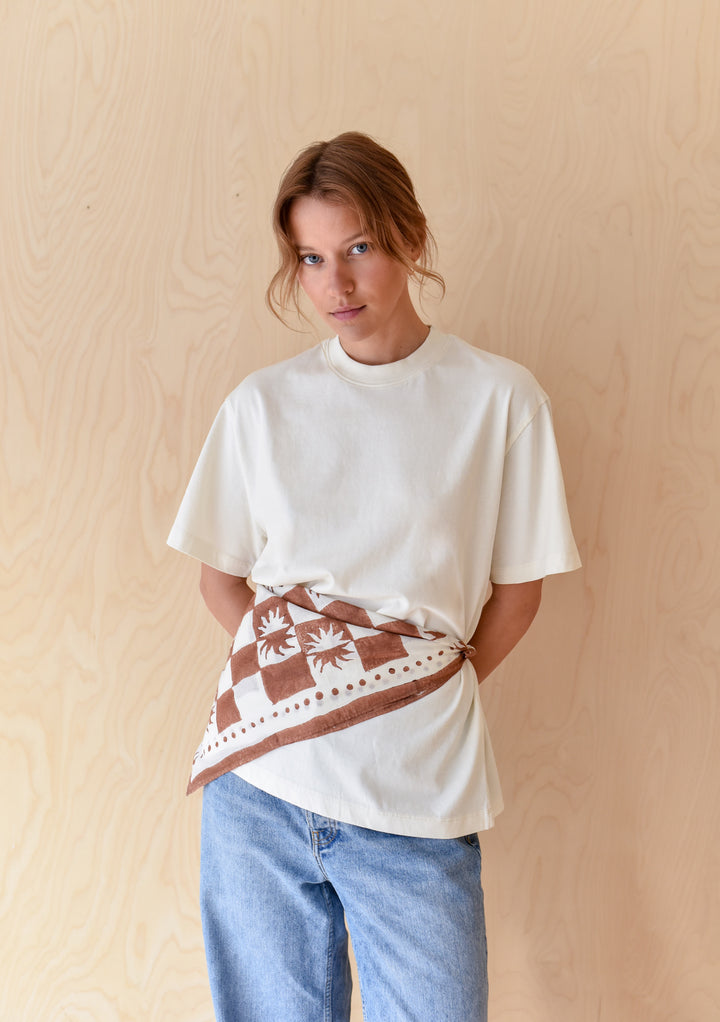 Young woman in jeans and off-white T-shirt wears The Artist Series TBCo x Frankie Penwill Cotton Scarf, featuring a brown and white geometric/palm design.