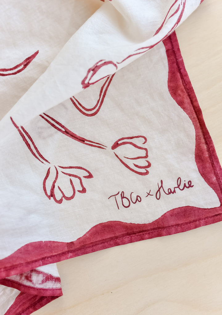 Close-up of TBCo x Harlie Briggs Artist Series cotton triangle neck scarf in white with red floral line art, featuring the TBCo x Harlie logo