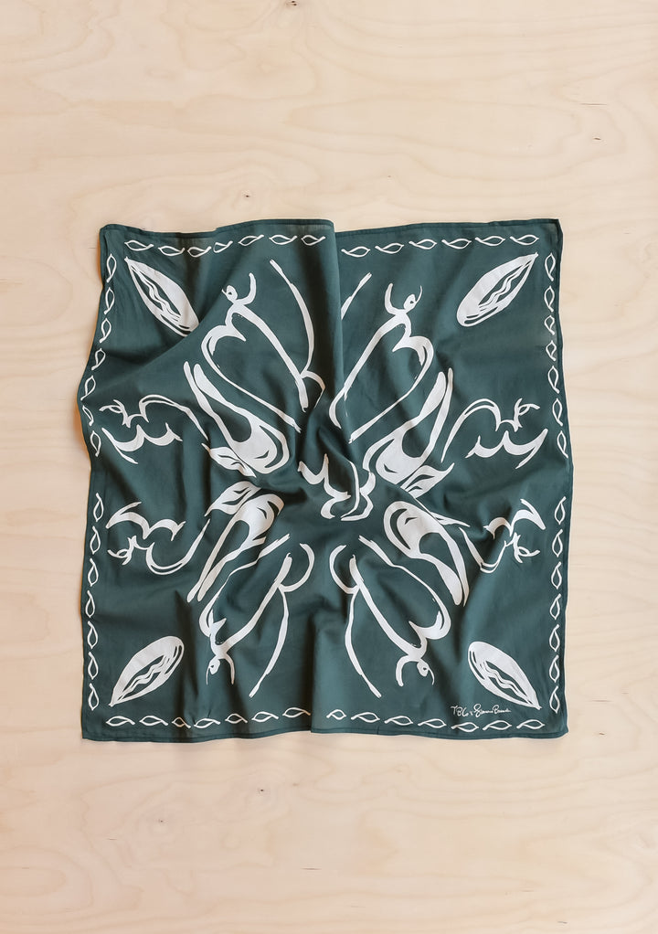 The Artist Series TBCo x Simone Brewster Cotton Scarf, featuring a deep green with white leaf motifs, laid flat on a wood surface.