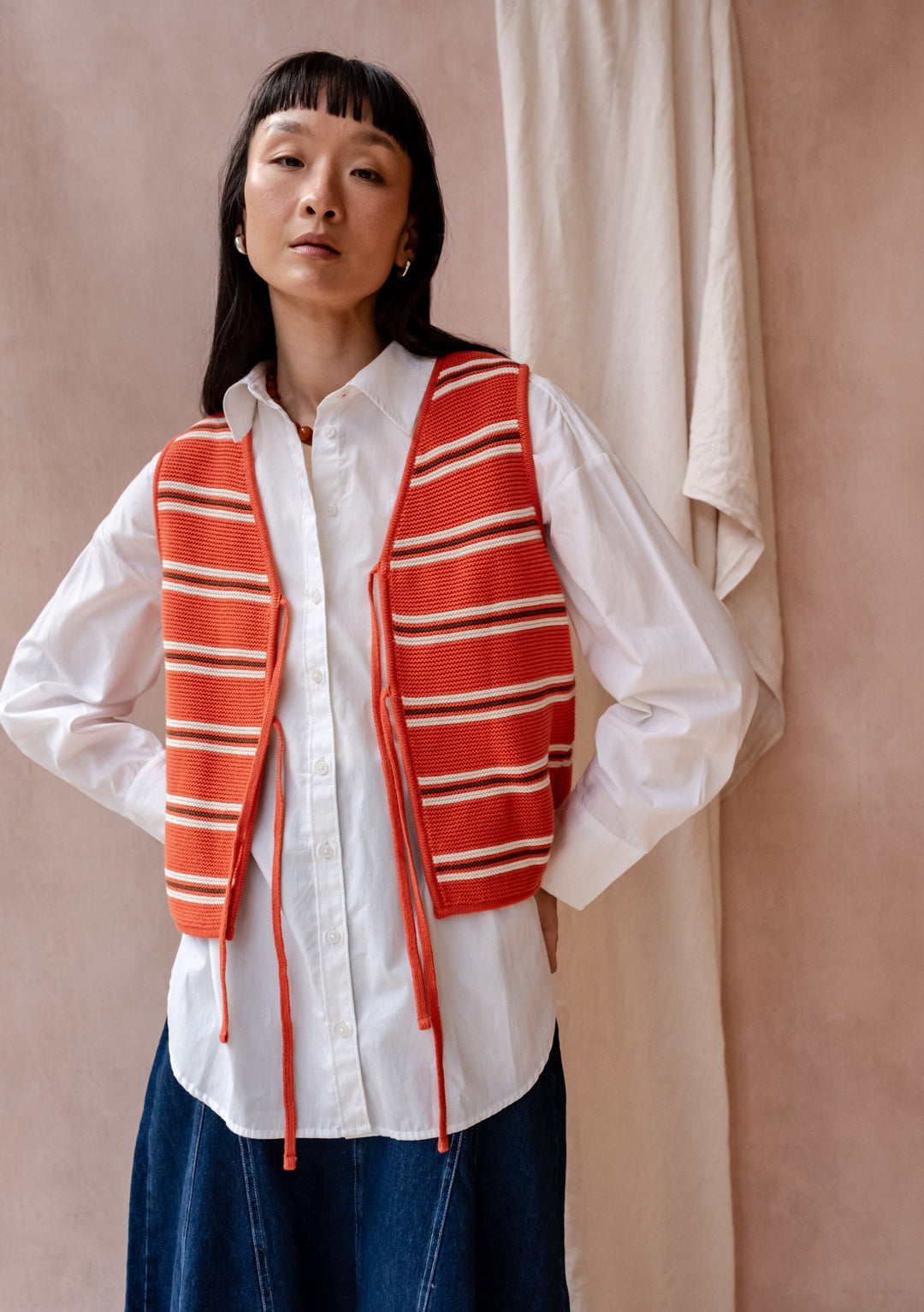 TBCo Cotton Knitted Vest in Tangerine Stripe shown styled with white button-down shirt and denim skirt against neutral backdrop