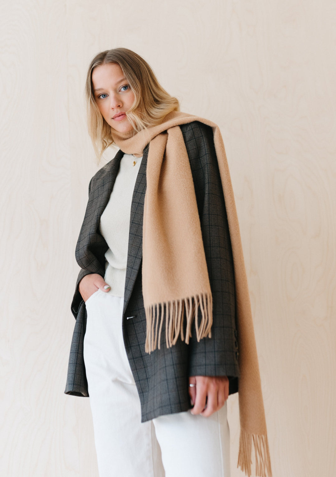 TBCo luxury camel cashmere scarf with fringe draped elegantly over grey checked blazer against neutral background