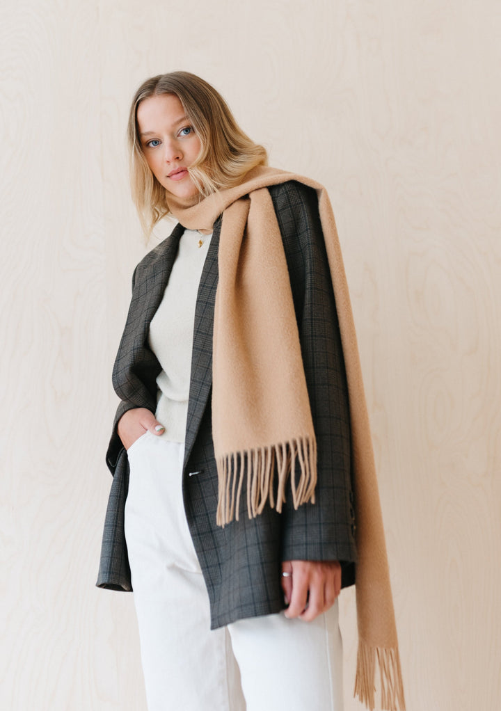TBCo luxury camel cashmere scarf with fringe draped elegantly over grey checked blazer against neutral background