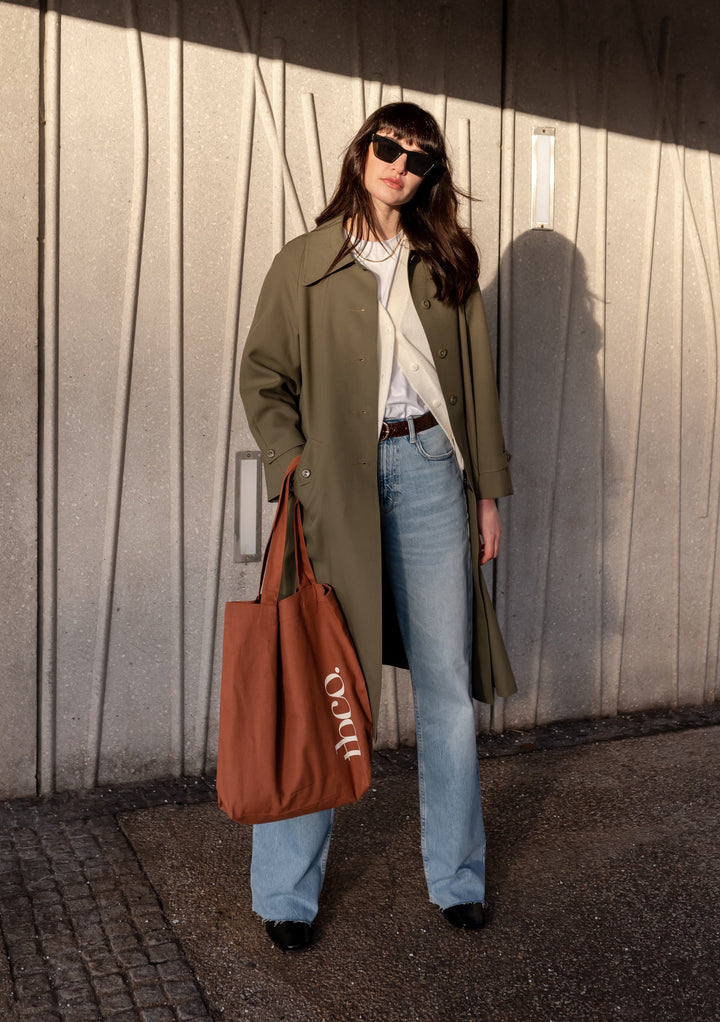 Stylish person carrying rust-coloured TBCo Recycled Cotton Tote with olive coat and denim, showcasing TBCo sustainable fashion