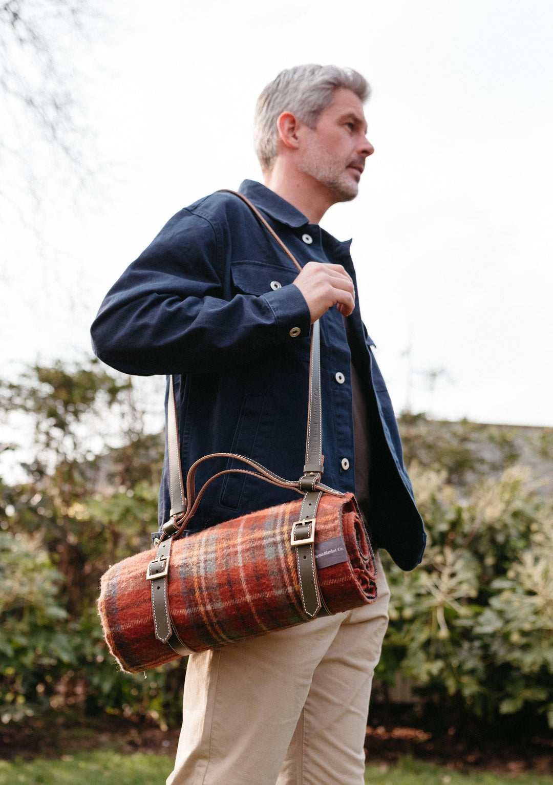 TBCo Leather Picnic Carrier with adjustable shoulder strap shown in brown leather with tartan wool blanket roll outdoors