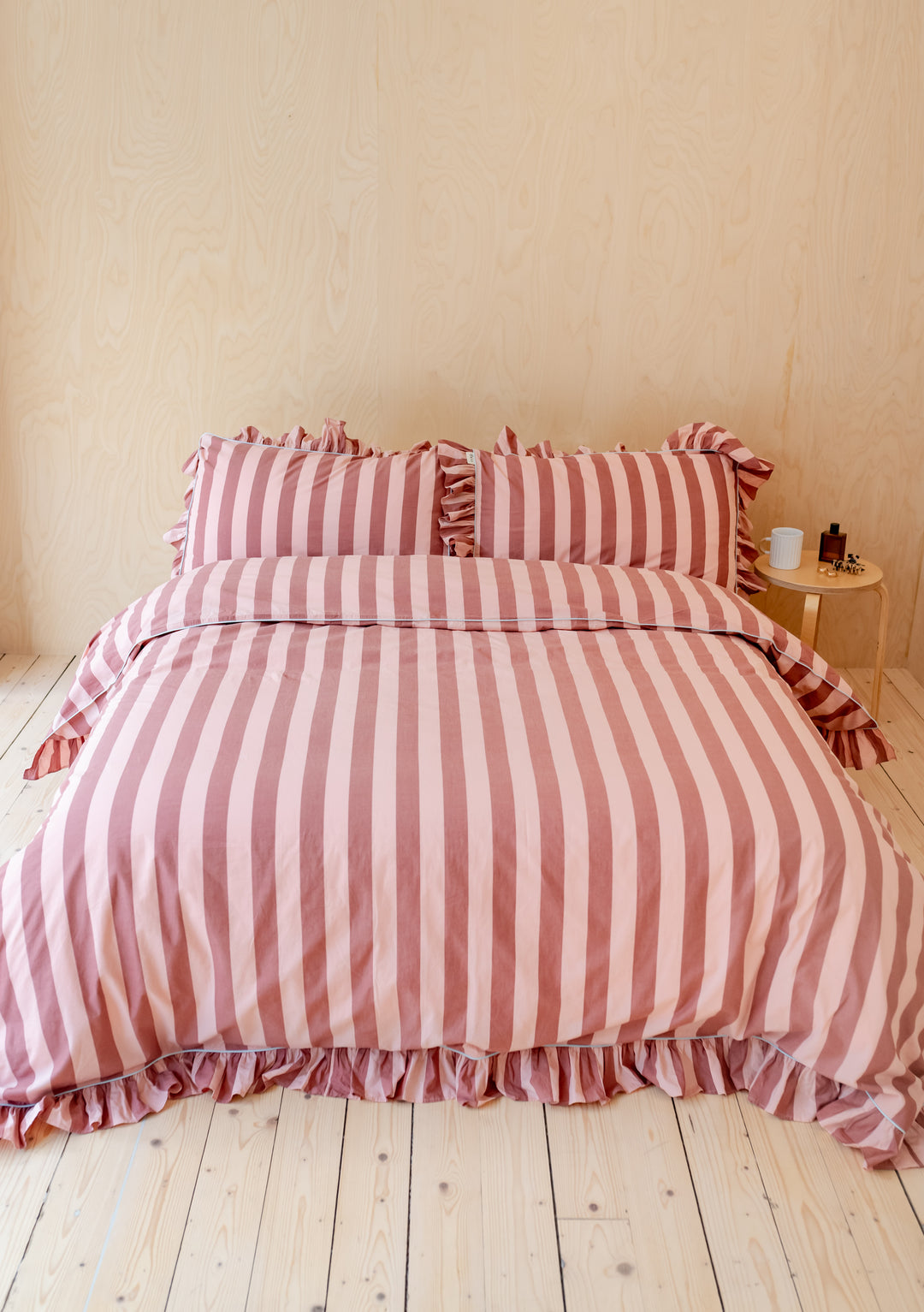 TBCo Cotton Duvet Cover in pink and red stripes with ruffled edges displayed on wooden floor beside bedside table