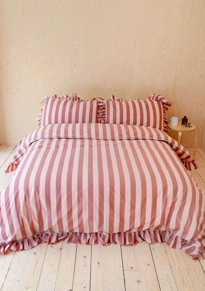 TBCo Cotton Duvet Cover in pink and red stripes with ruffled edges displayed on wooden floor beside bedside table