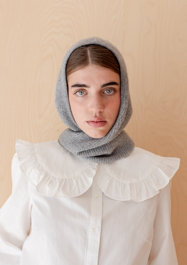 Model wearing a grey two-tone Merino Hood by TBCo styled over a white blouse with ruffled collar against a wood background