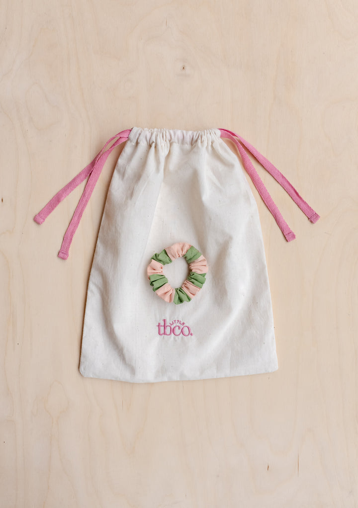 Cotton drawstring bag with pink ribbons and TBCo embroidered logo, featuring green and pink striped scrunchie detail