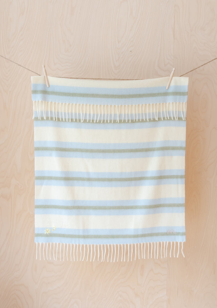 TBCo Lambswool Baby Blanket in blue and cream stripes with fringed edges, featuring sun and moon embroidery detail