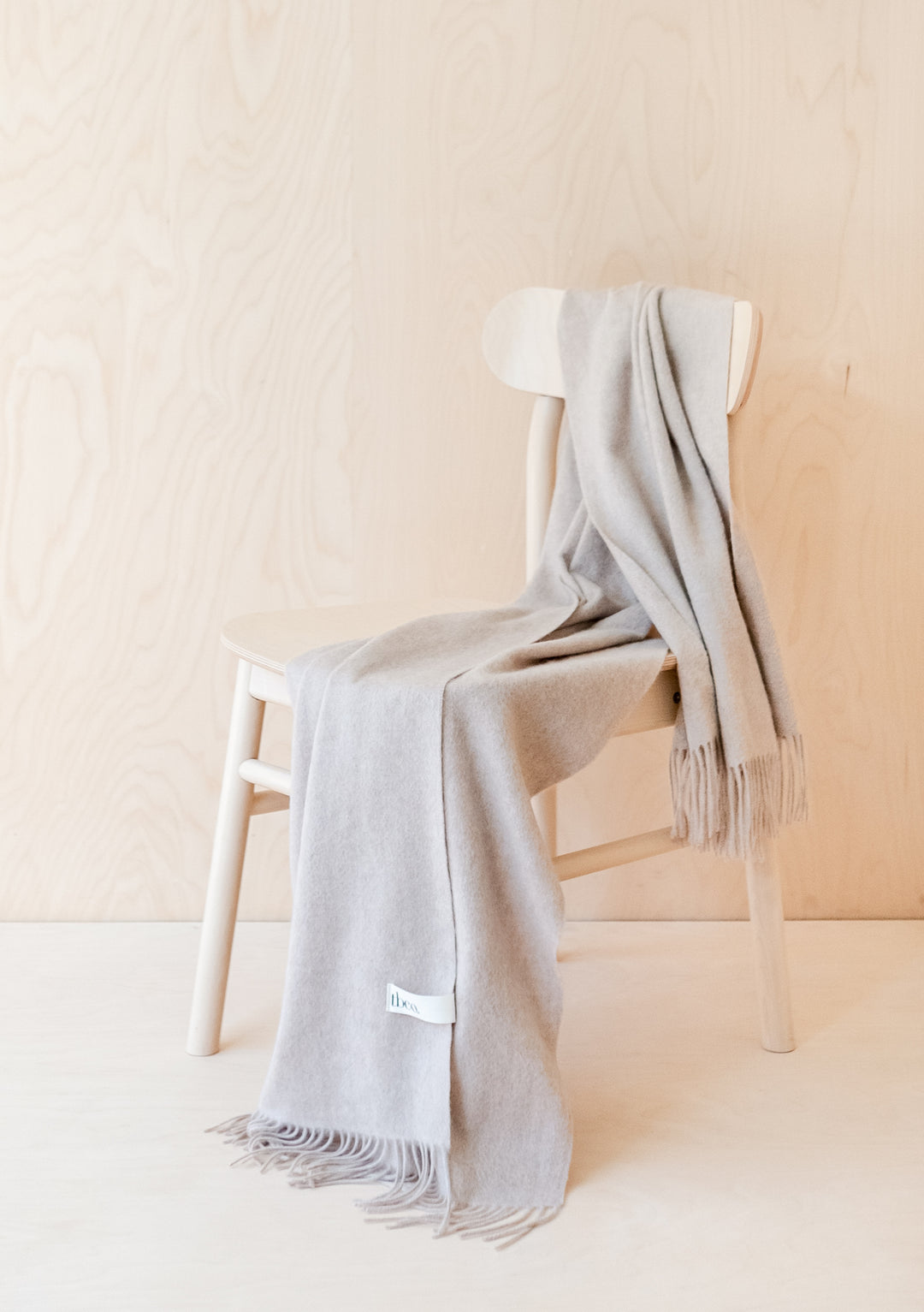 TBCo Cashmere Small Blanket in Oatmeal Melange elegantly draped over white chair, showcasing fringed edges and luxurious texture
