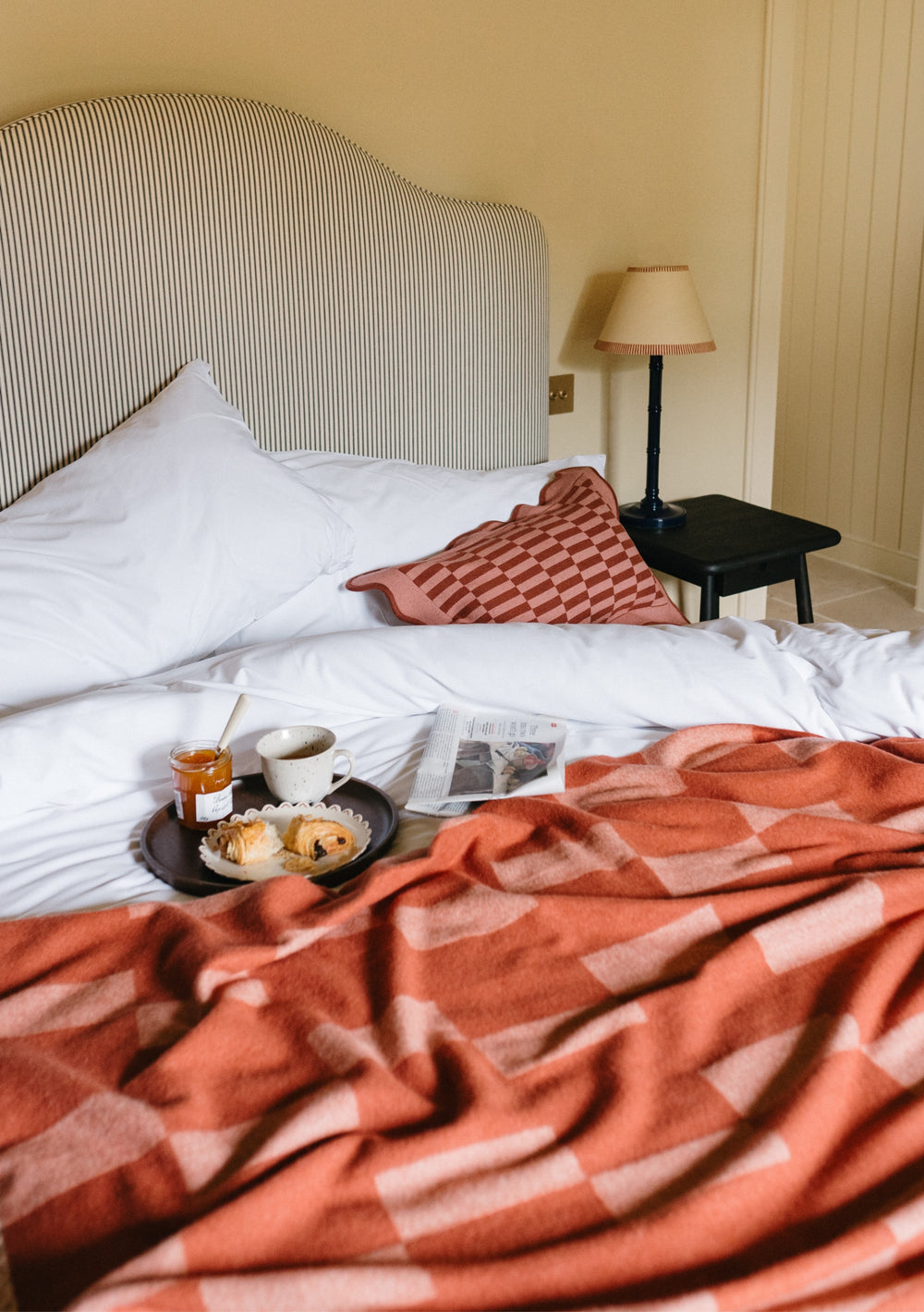 TBCo Lambswool Blanket in Apricot Checker draped over white bedding with breakfast tray, showcasing cosy bedroom setting