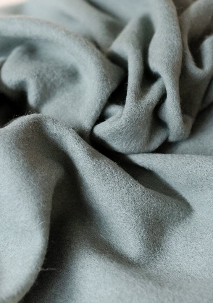 Soft folds of TBCo Lambswool Blanket in Sage Melange showcasing luxurious texture and gentle sage green colour