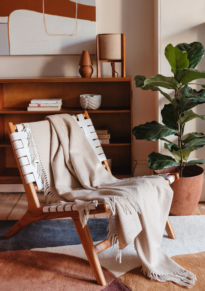 TBCo Recycled Wool Waffle Blanket in Camel draped over wooden lounge chair beside indoor plant and terracotta decor
