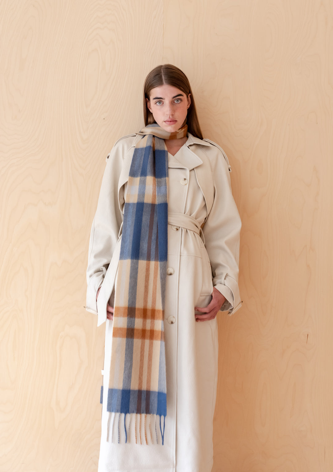 Model wearing TBCo Lambswool Skinny Scarf in Camel Modern Tartan with a light trench coat against wooden background