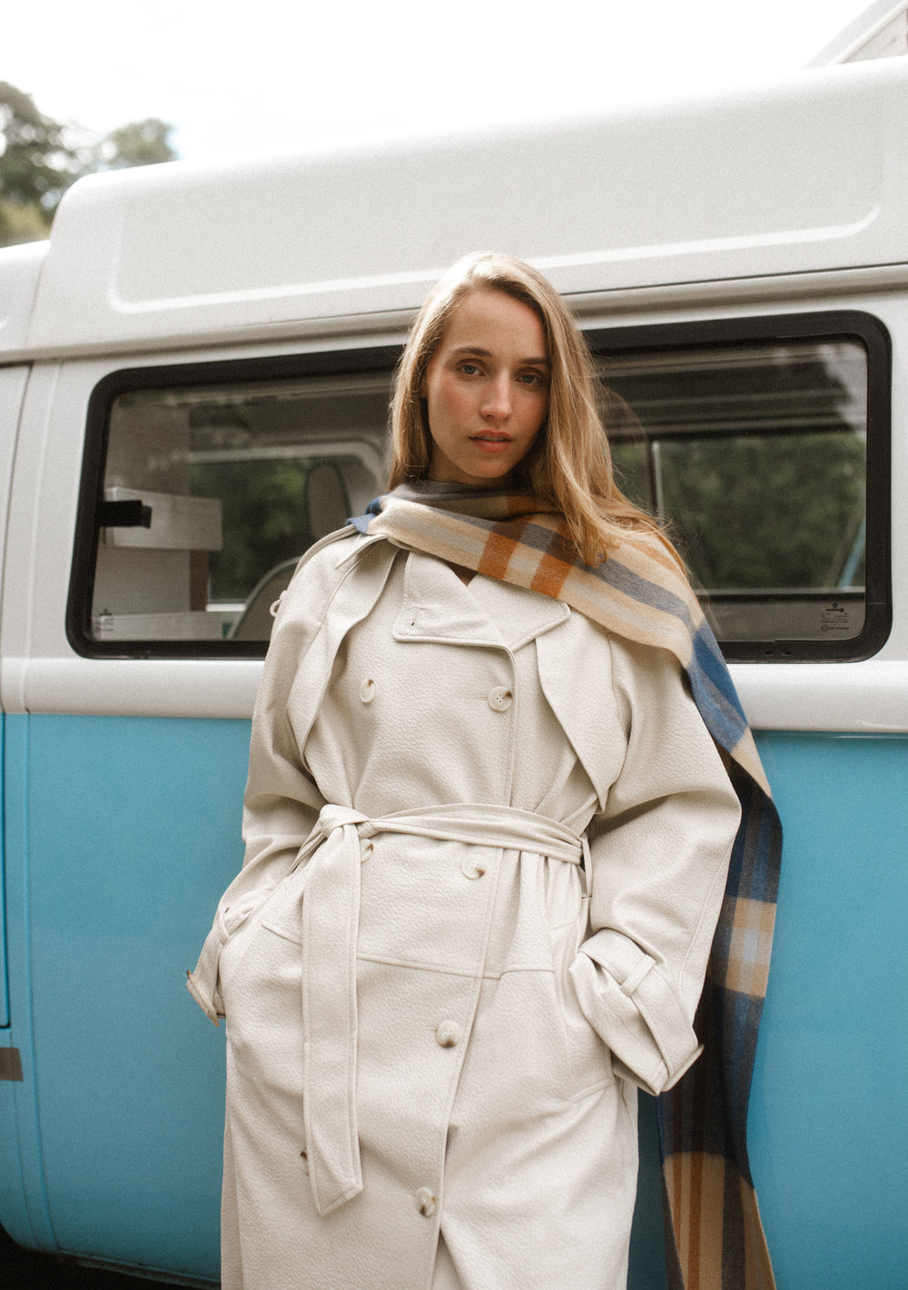Woman wearing TBCo Lambswool Skinny Scarf in Camel Modern Tartan over cream trench coat standing by blue van outdoors
