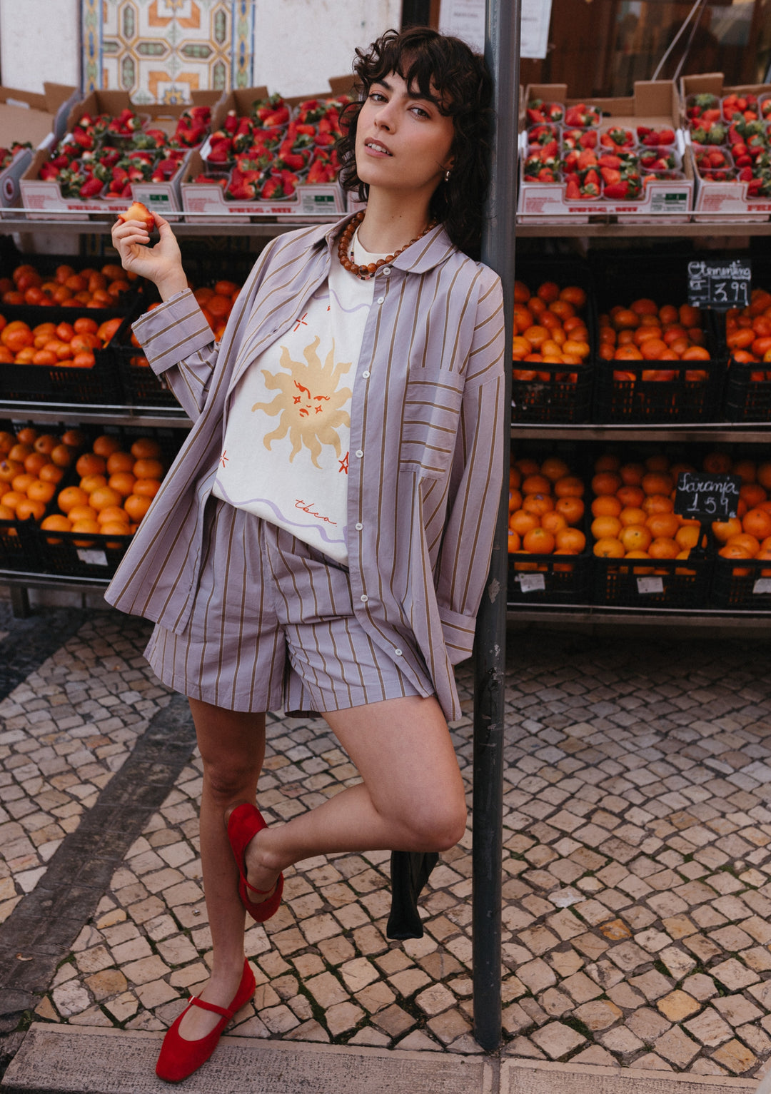 Cotton Shirt in Lilac Stripe by TBCo shown as oversized fit with olive stripes, displayed at market fruit stand setting
