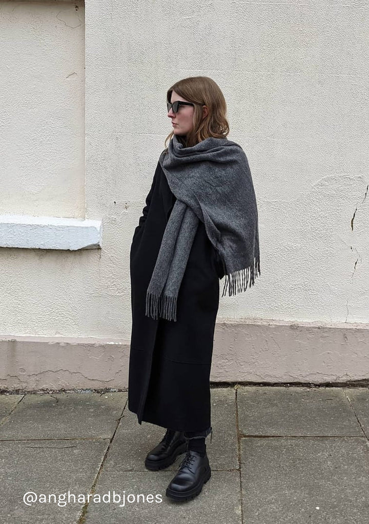 TBCo oversized lambswool scarf in charcoal melange styled as a wrap over black winter coat on urban street setting