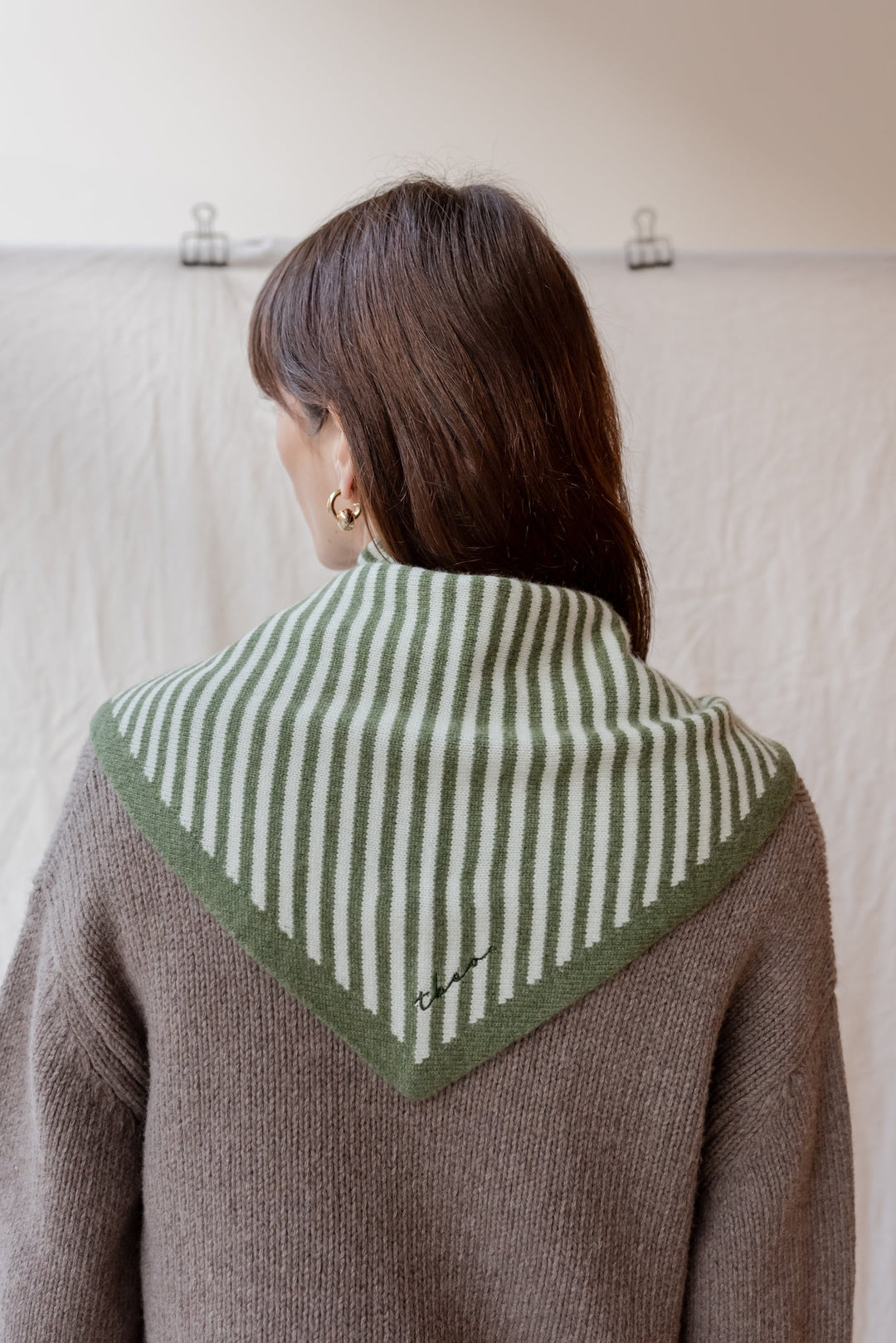 Model wearing TBCo large Merino triangle scarf in green stripe pattern, styled with grey cardigan, showing back view