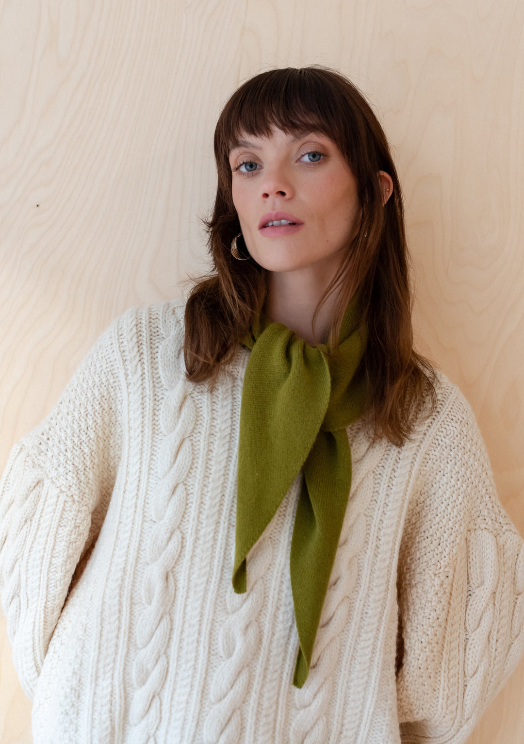 Olive merino wool TBCo triangle scarf styled with cream cable knit jumper showing versatile styling against natural wood background