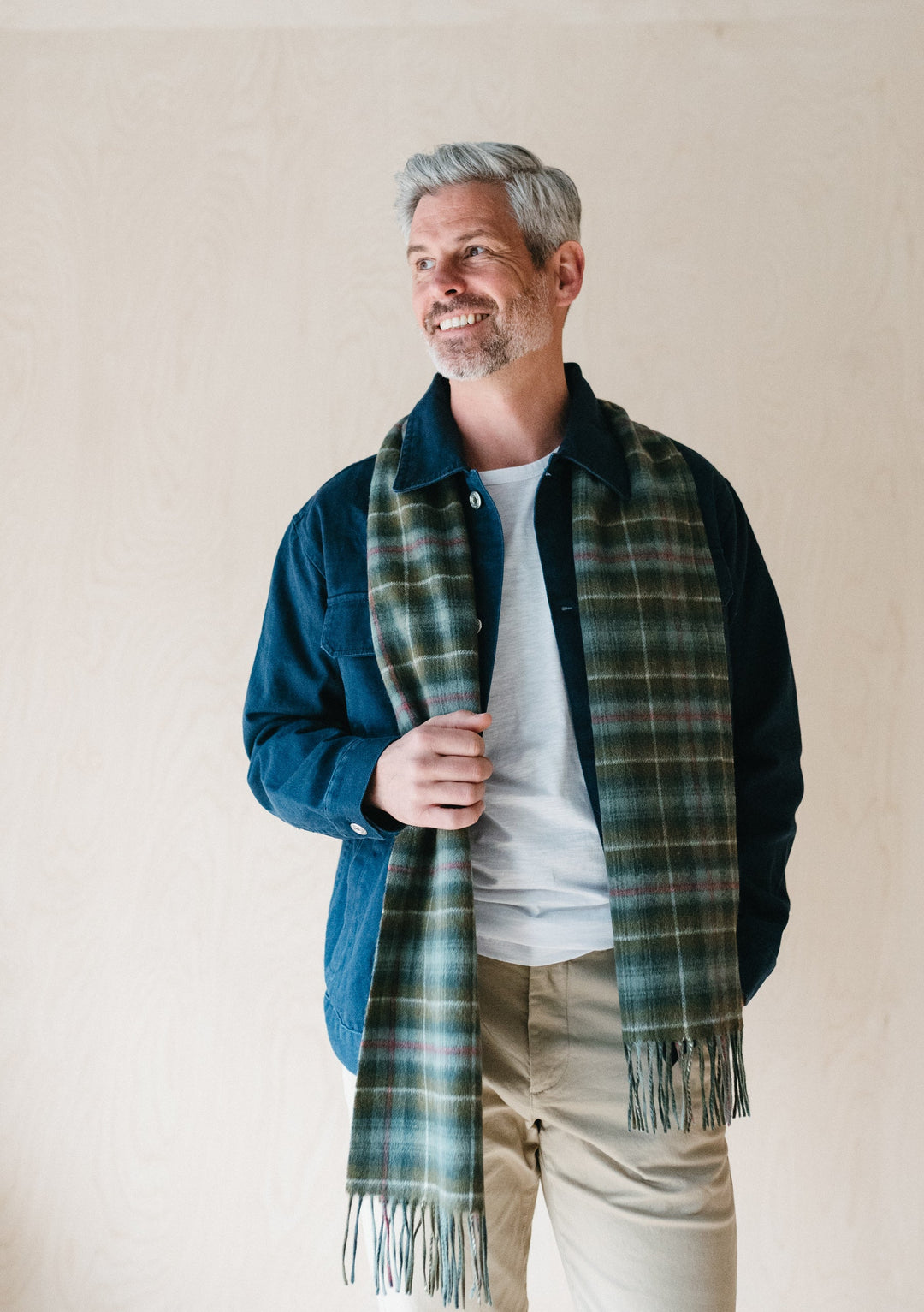 TBCo Men's Lambswool Scarf in Mackenzie Weathered Tartan styled casually with denim jacket and white t-shirt against neutral wall