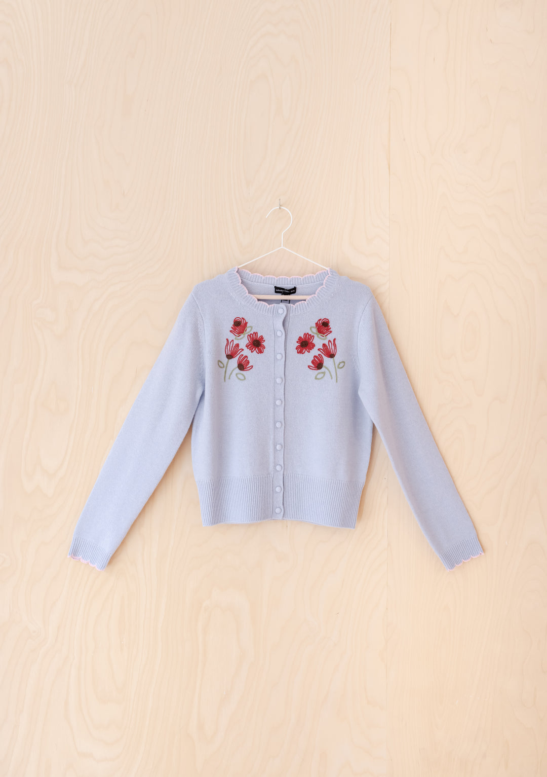 The Nobody's Child x TBCo Blue Floral Wool Cardigan features light blue wool, long sleeves, front buttons, and pink-red floral embroidery on the chest—an eco-friendly, stylish knitwear piece perfect for any occasion.