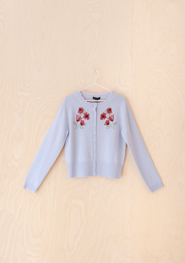 The Nobody's Child x TBCo Blue Floral Wool Cardigan features light blue wool, long sleeves, front buttons, and pink-red floral embroidery on the chest—an eco-friendly, stylish knitwear piece perfect for any occasion.