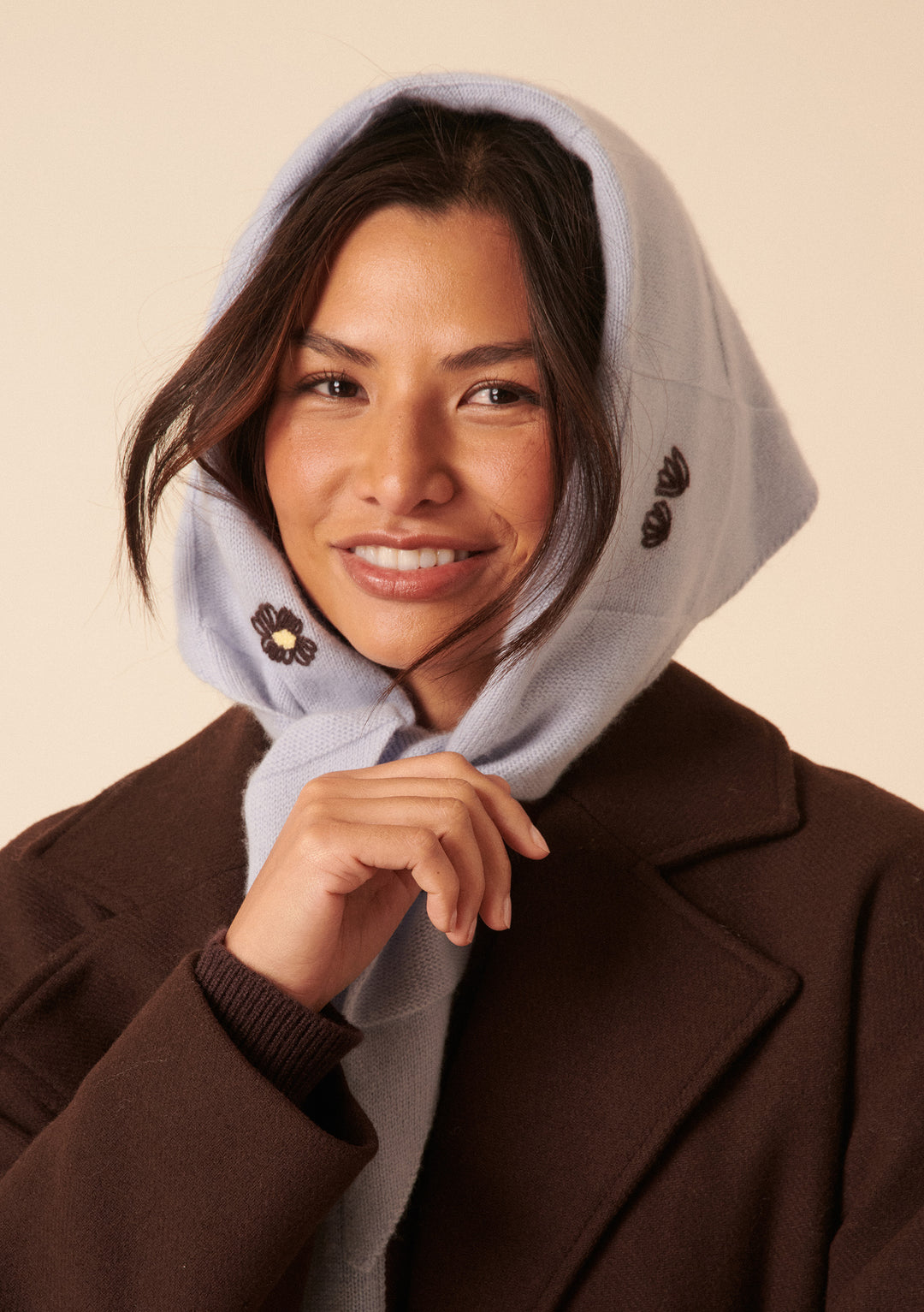 Smiling woman wears the NC x TBCo Blue Floral Wool Triangle Scarf tied under the chin over a brown coat