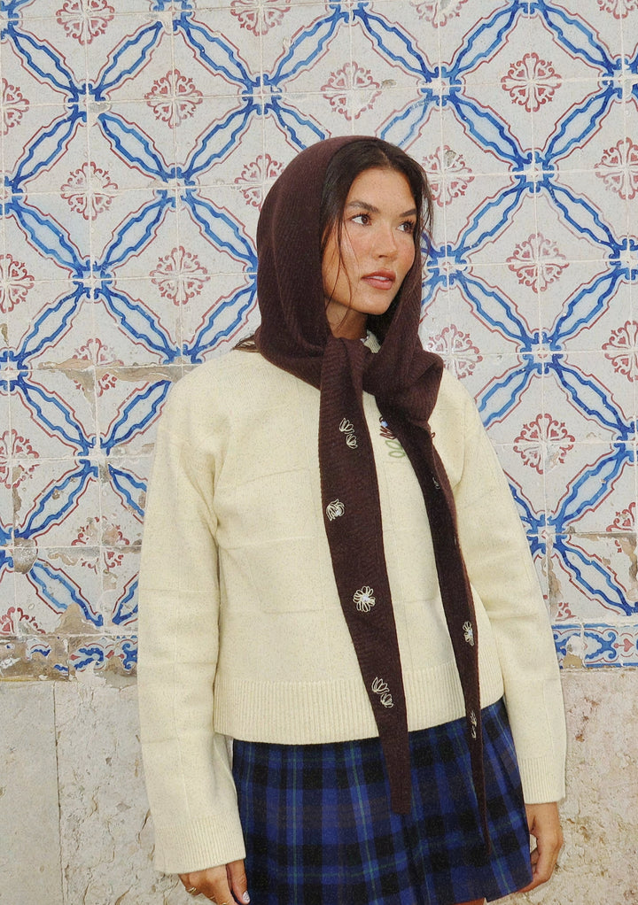 Woman wearing NC x TBCo Latte Floral Wool Hood with embroidered flowers styled with cream jumper and blue plaid skirt
