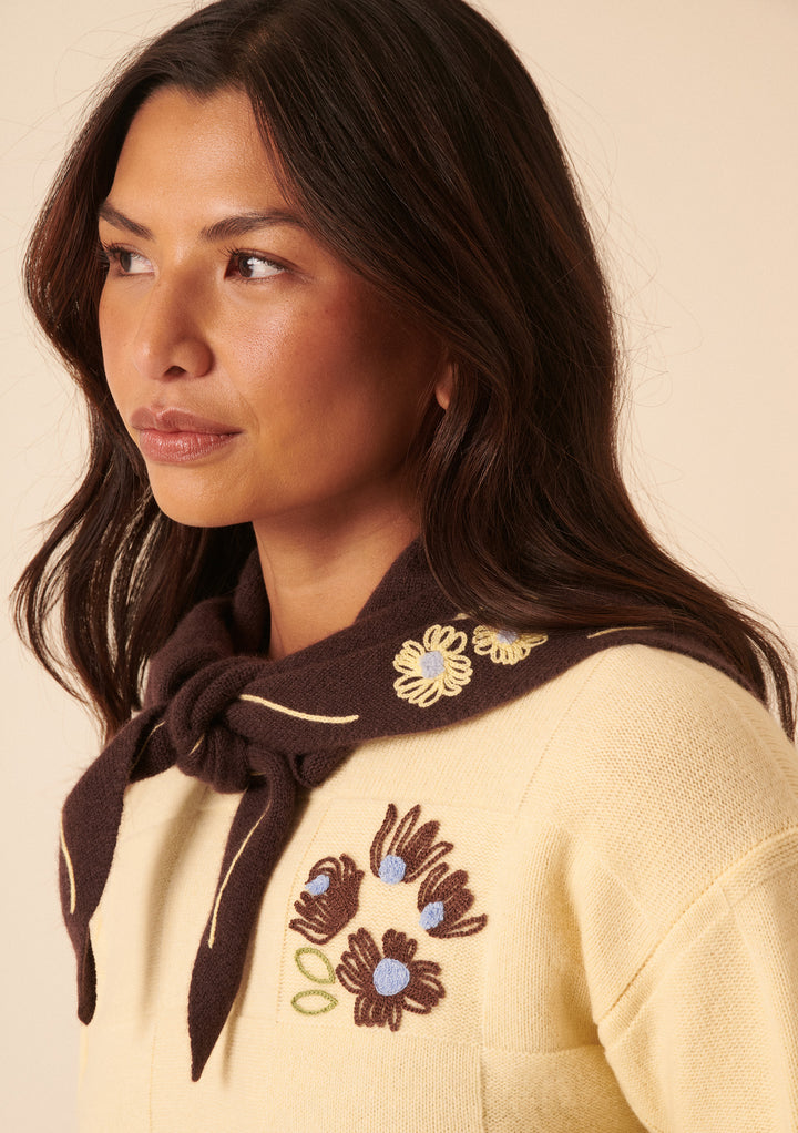 Woman wearing NC x TBCo Latte Floral Wool Triangle Scarf with yellow embroidery tied around neck over cream jumper
