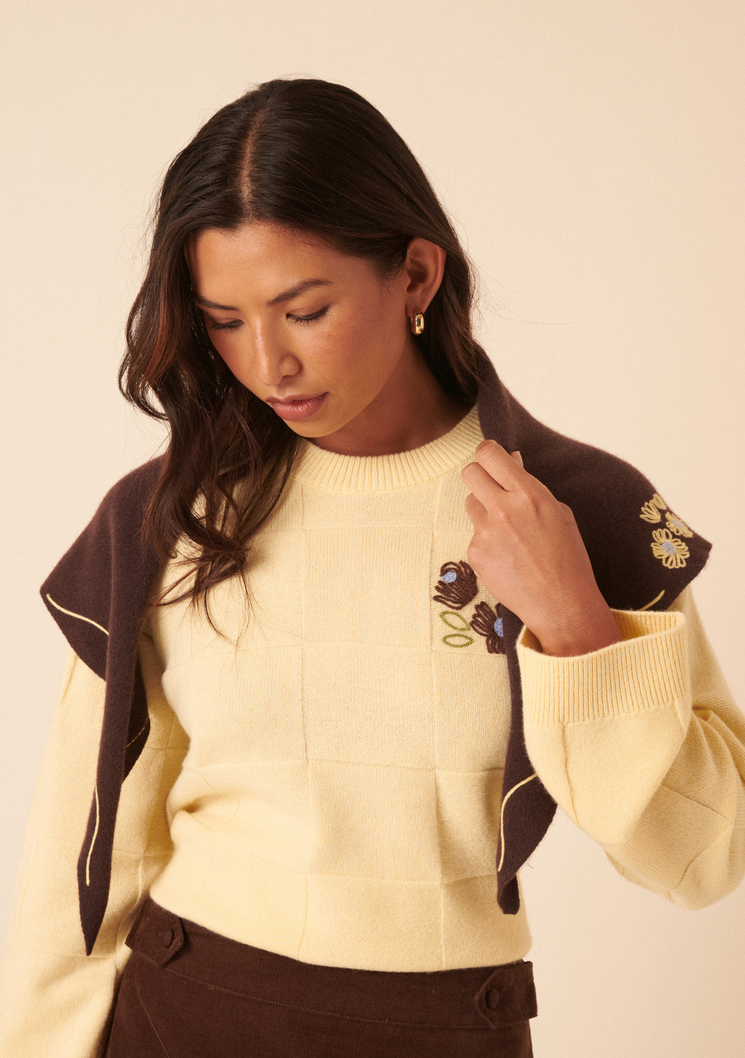 Woman wearing the NC x TBCo Latte Floral Wool Triangle Scarf with delicate yellow floral embroidery by TBCo.