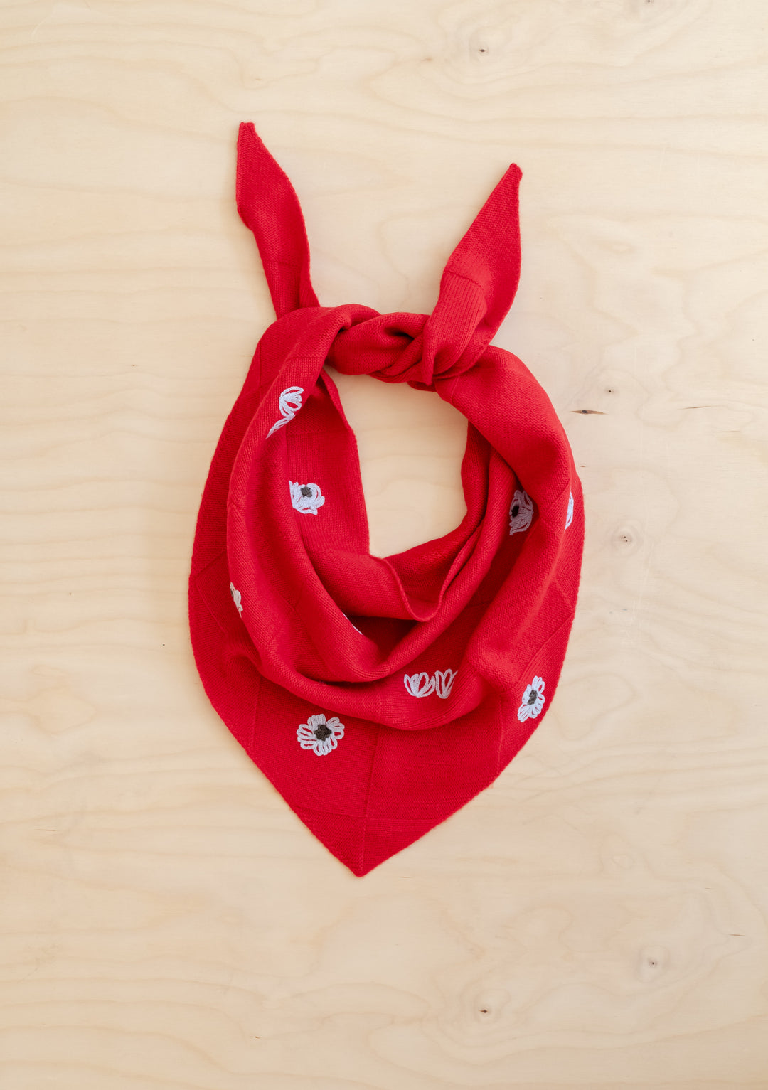 NC x TBCo Red Floral Wool Triangle Scarf knitted from soft merino wool with blue floral embroidery detail on light wooden background