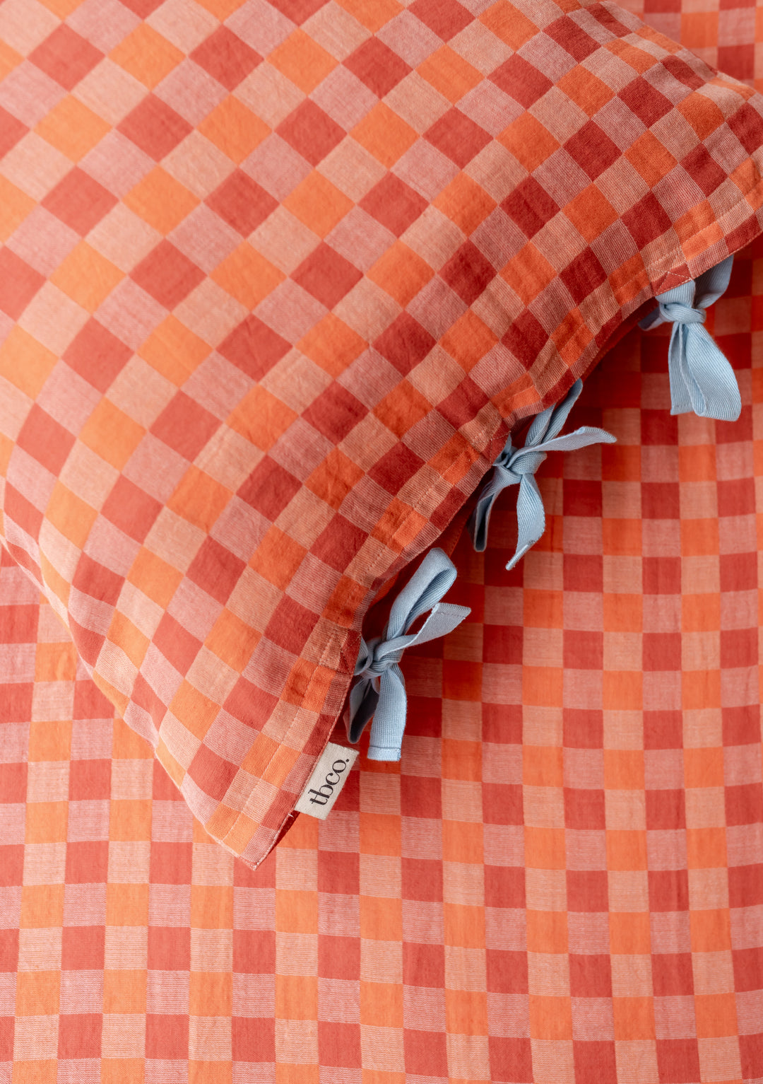 TBCo cotton pillowcases in apricot checkerboard pattern with blue tie closures, showcasing soft woven texture and elegant design