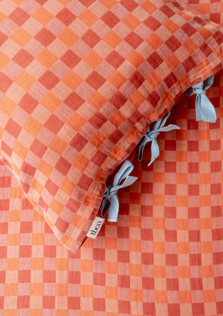 TBCo cotton pillowcases in apricot checkerboard pattern with blue tie closures, showcasing soft woven texture and elegant design