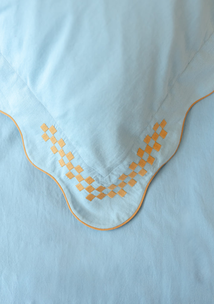 TBCo Cotton & Linen Pillowcases in Blue with scalloped edges and camel checkerboard embroidery detail, close-up of corner design