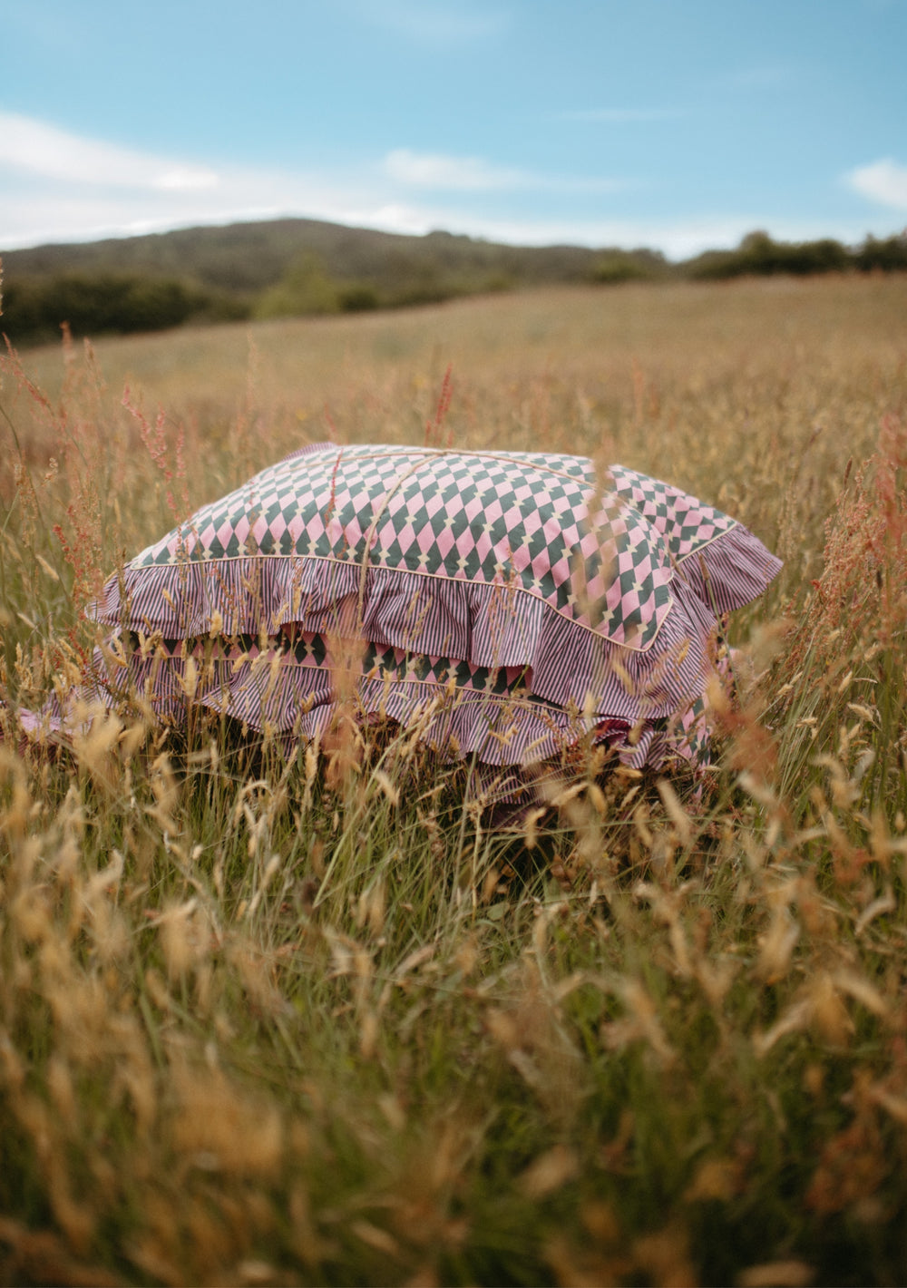 Pair of Cotton Pillowcases in Pink Harlequin by TBCo with soft cotton and ruffled edges in a grassy field setting