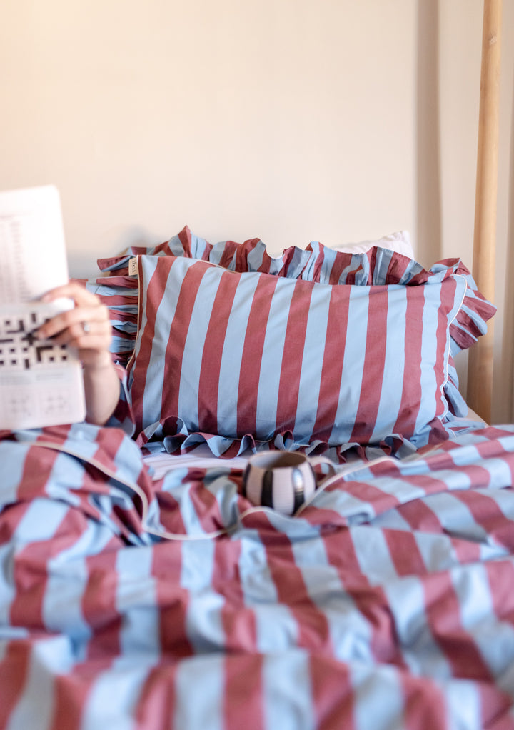 TBCo Cotton Pillowcases with blue and red stripes featuring ruffled edges, shown on a cosy bed setting in natural light