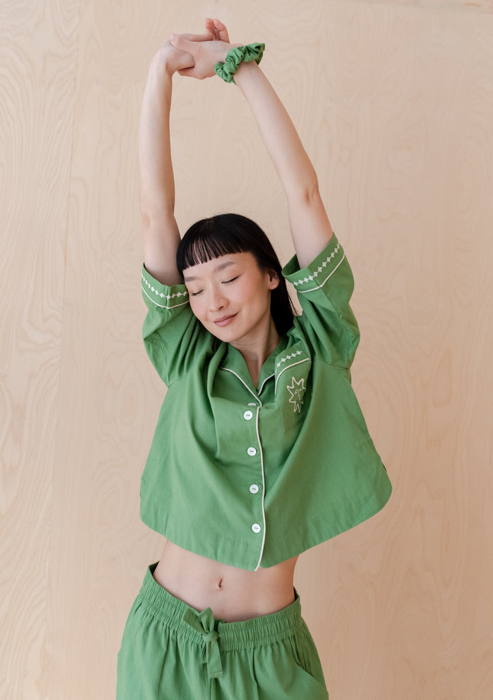 A person stretching in TBCo Cotton & Linen Pyjamas in green, featuring embroidered details and matching scrunchie