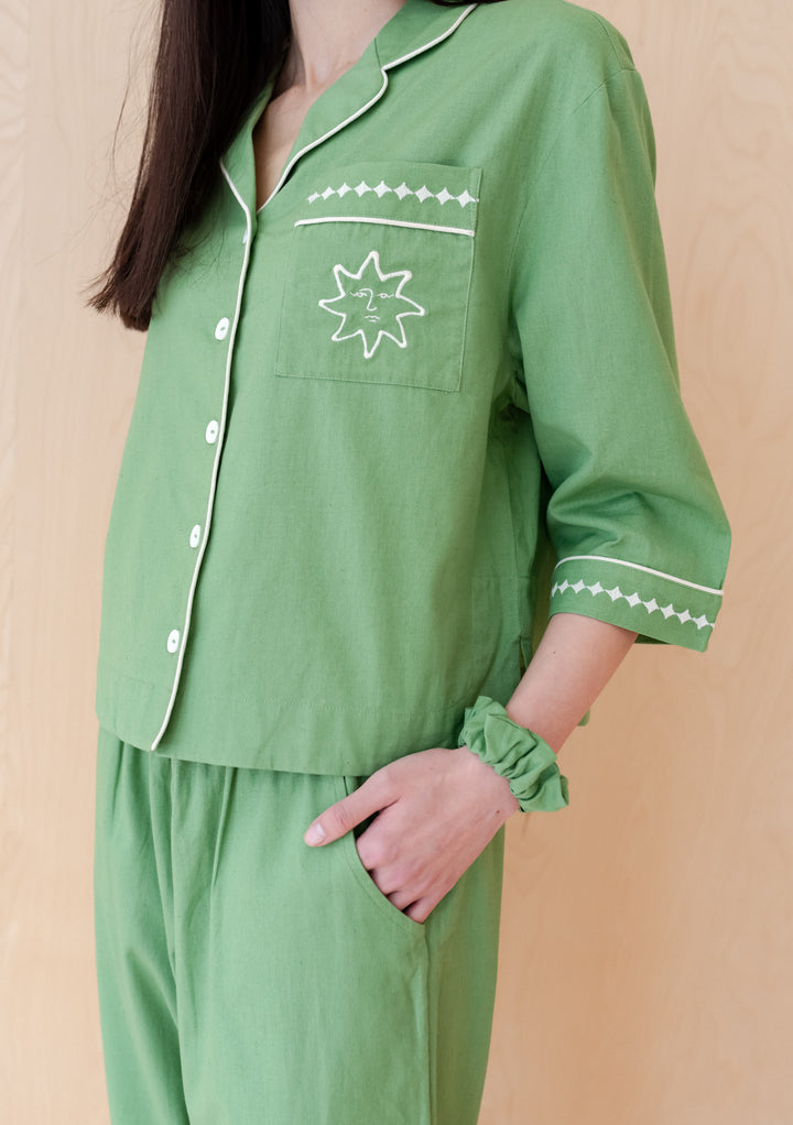 Soft green TBCo Cotton & Linen Pyjamas with embroidered sun motif pocket and white trim detail, styled with matching scrunchie