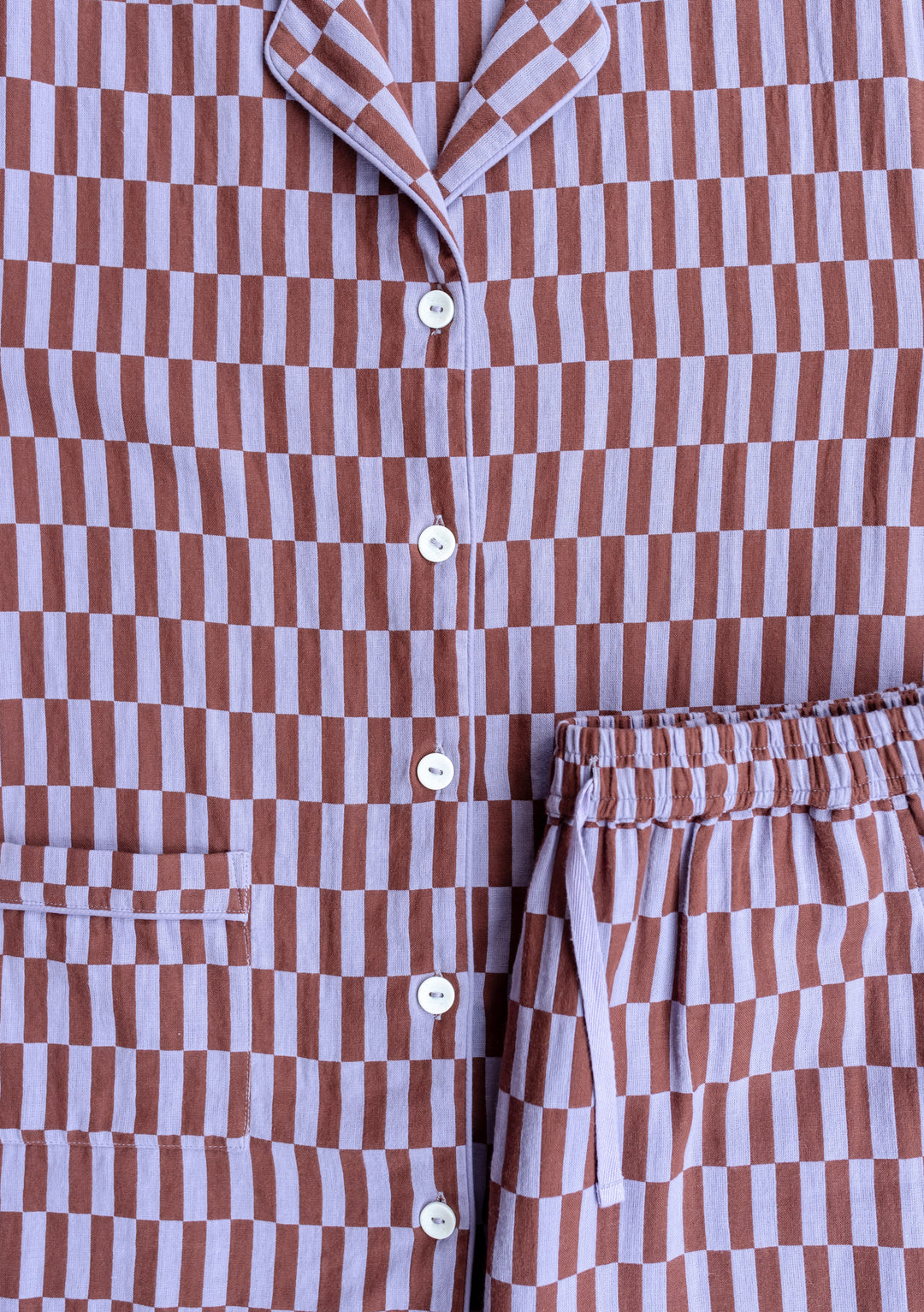 Close-up detail of TBCo Cotton Pyjamas in Lilac Checkerboard pattern, showing button placket and elasticated waist with matching print