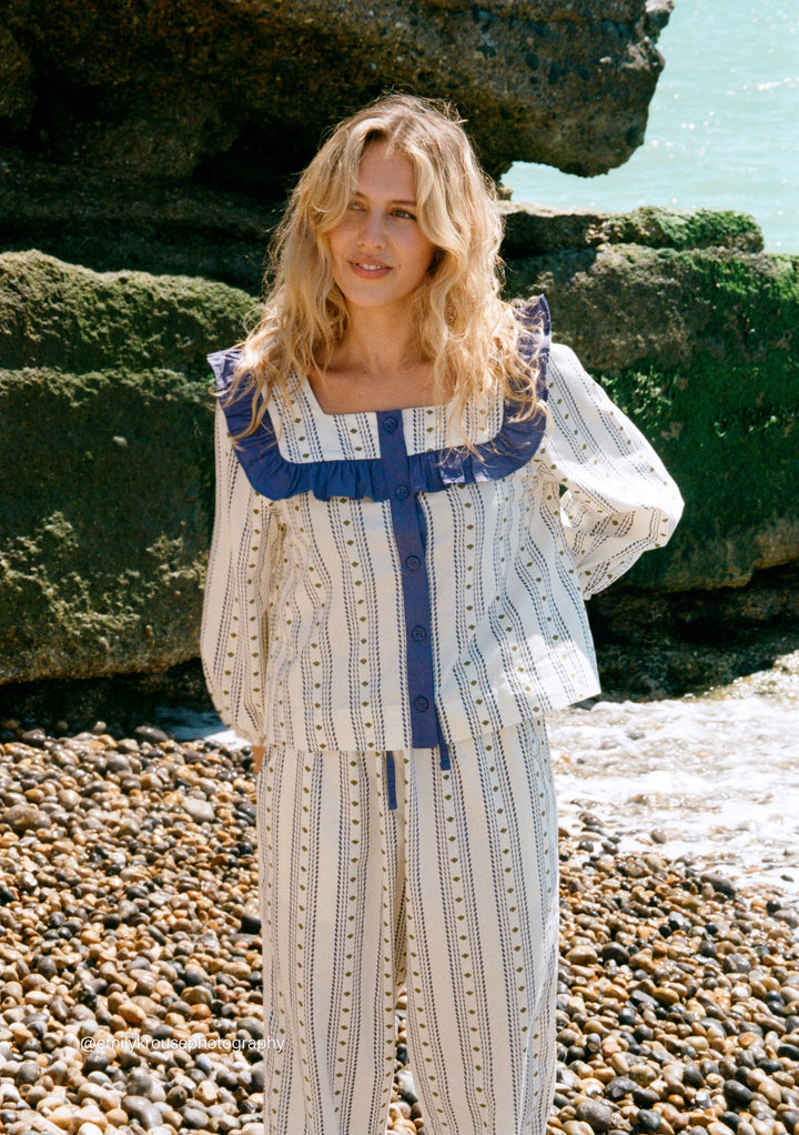 Woman wearing TBCo Cotton Pyjamas in Navy Ditsy floral with ruffle collar and cropped trousers by the shore